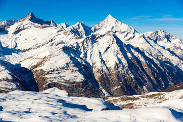 Picturesque landscape of Pennine Alps highlands around Zermatt with snow-capped rocky mountain ranges and marked ski trails on sunny winter day, Switzerland