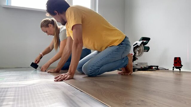 A family of woman and man install laminate on the floor in their apartment. DIY concept. Slowmotion video