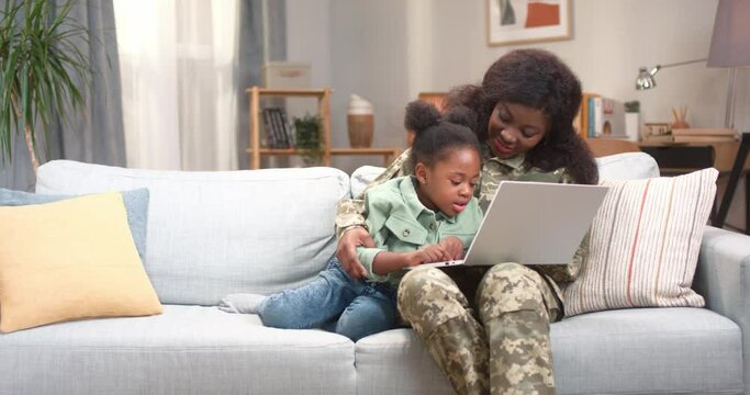 African woman in army uniform using laptop with daughter