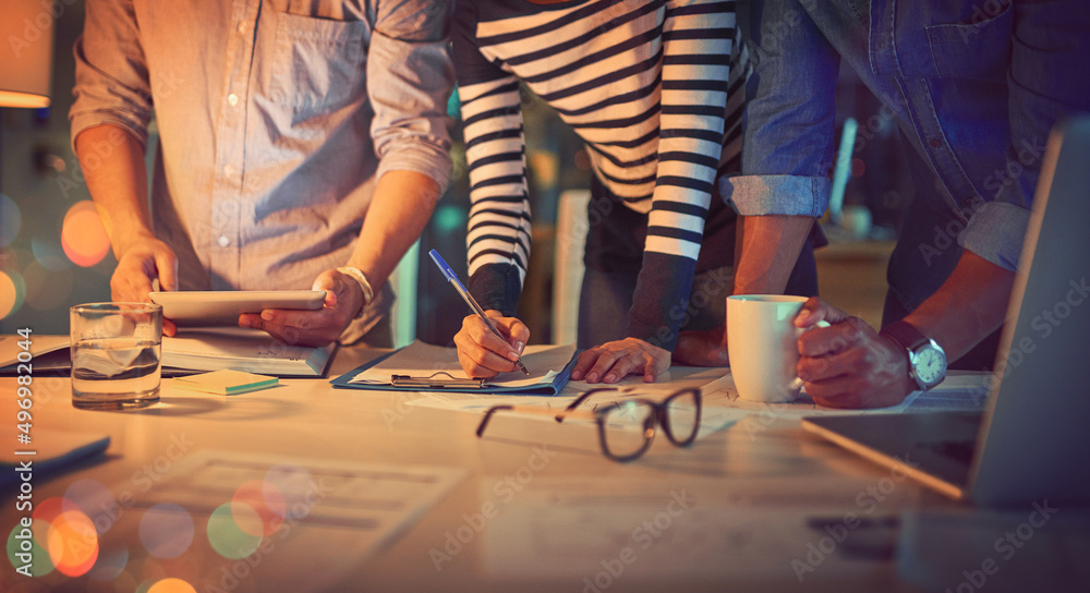 Poster coordinating their ideas together. shot of a group of unrecognizable designers working late in an of