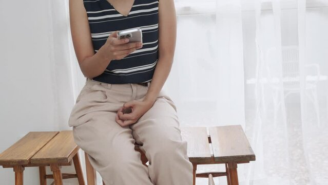 Close up 4K of unrecognised asian young woman who is holding and using her smartphone to connect people by using internet technology in bright and comfortable living room for modern lifestyle.
