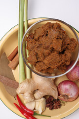 Traditional cooked beef meat rendang dry curry closeup in transparent glass bowl with ingredients onion ginger lemon grass bay leaf cardamom clove cinnamon garlic chilli star anise