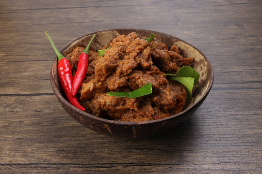 Traditional cooked dry curry beef meat rendang closeup in coconut shell bowl on rustic wooden background