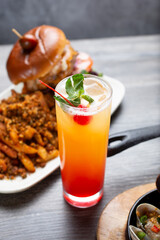 A view of a tequila sunrise cocktail, next to some appetizers and entrees.