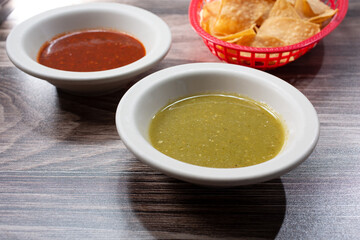 A view of condiment cups of salsa next to a basket of tortilla chips.
