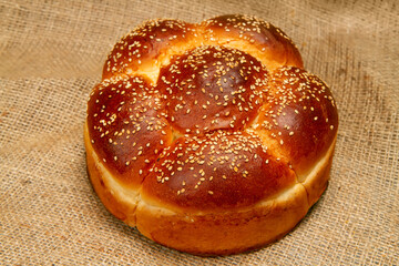 A round loaf of sweet bread with sesame against the background of burlap.