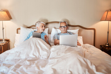 Learning how to operate technology in the 21st century. Cropped shot of a senior couple sitting in bed together and using technology in a nursing home. - Powered by Adobe