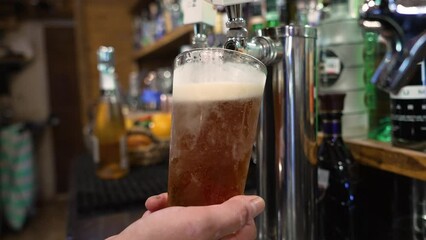 Bartender fills frosted pint glass with cold draft beer, slow motion close up 4K
