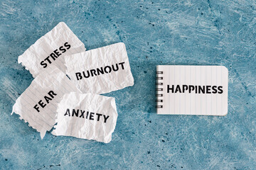 Happiness text on notepad surrounded by Fear Anxiety Stress and Burnout words on torn scrunched up pages, psychology and overcoming your past obstacles