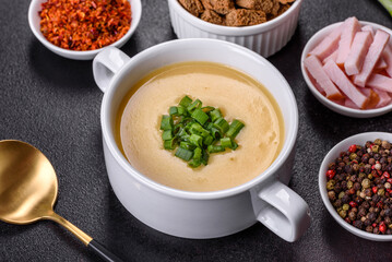 Cream soup with potatoes, leek and peas on a dark concrete table