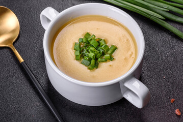 Cream soup with potatoes, leek and peas on a dark concrete table