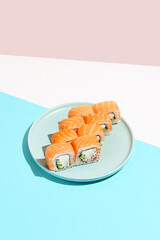 Classic sushi roll with salmon outside, crab, cheese and cucumber inside. Philadelphia maki in minimal style. Modern japanese menu concept. Salmon maki roll on ceramic plate on coloured background.