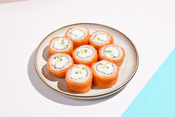 Philadelphia maki roll on ceramic plate with chopsticks. Salmon sushi roll with philadelphia cheese on coloured background. Japanese menu concept. Salmon sushi roll in modern style.