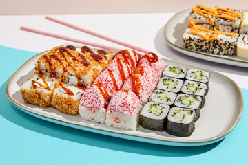Sushi set on ceramic dishware with coloured chopsticks. Trendy set of maki sushi in minimal style. Modern japanese menu concept. Maki sushi assorted on coloured background.