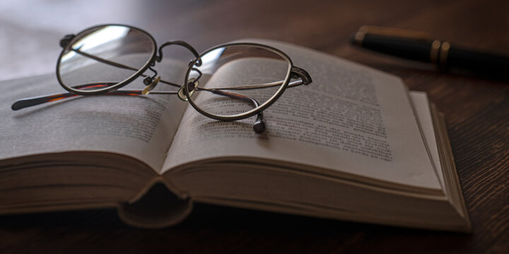 開かれた本、眼鏡、万年筆。読書、勉強などのイメージ。