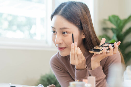 Beauty blogger concept, beautiful and cute asian young woman, girl makeup face by applying brush for eyes on eyebrow, eyeshadow looking at the mirror at home. Female look with natural fashion style.