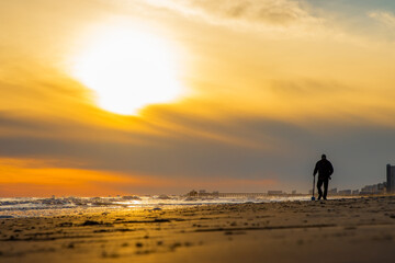 Man with metal detector walking on beach at sunset