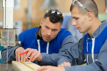 carpenter showing apprentice how to use sawing machine