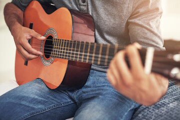 He lets the music flow from his hands. Shot of an unrecognizable man practising guitar at home.