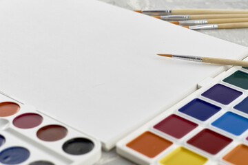 watercolor paints brush and sketchbook on a gray textured surface