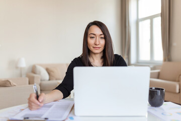 Asian woman working on laptop computer, smiling. Woman Working From Home On Laptop In Modern Apartment. Trendy woman working on laptop from home