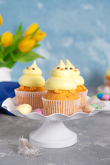 Cute Easter chick cupcakes. Vanilla cupcakes with buttercream on a white stand with fresh flowers on a white wooden background. Copy space.