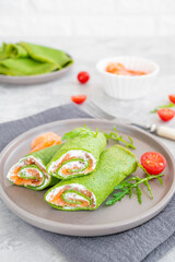 Green spinach crepes or pancakes with smoked salmon and soft cheese on a plate on the gray background. Copy space.