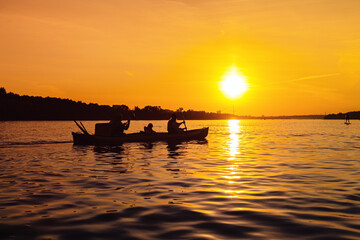 Silhouettes of people in boat at sunset. Family from mom, dad and child ride boat on river. Small family trip