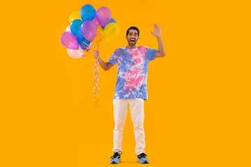 Happy young man holding bunch of balloons and gesturing with palm
