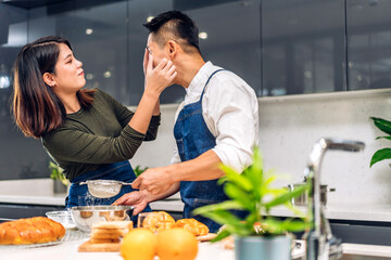 Young asian family couple having fun cooking together with dough for homemade bake cookie and cake ingredient on table.Happy couple looking to preparing food the dough in kitchen
