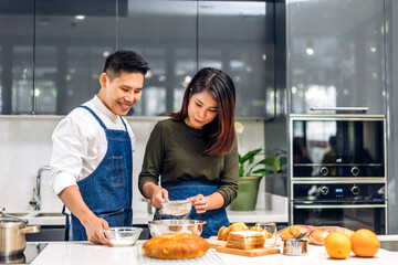 Young asian family couple having fun cooking together with dough for homemade bake cookie and cake ingredient on table.Happy couple looking to preparing food the dough in kitchen