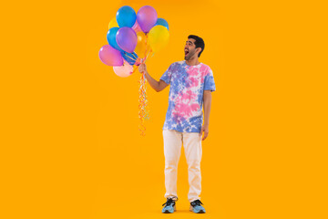Happy young man in colourful t-shirt holding bunch of balloons in hand