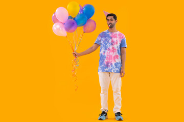 Sad young man holding balloons in hand and blowing party horn