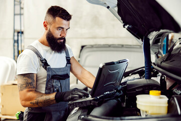 An auto-mechanic diagnostic a problem with vehicle at workshop on laptop. - obrazy, fototapety, plakaty