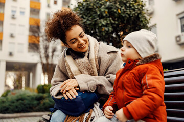 A happy young woman, caregiver or nanny, on a bench listening to the little boy talking.
