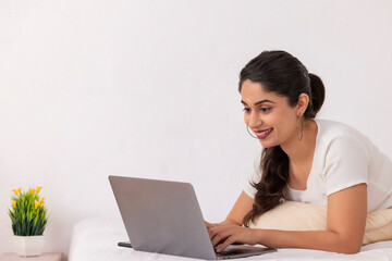 Portrait of young woman using laptop while lying down on bed at home