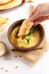 Chickpea snack hummus and a hand with a piece of pita, vertical frame on a light background.