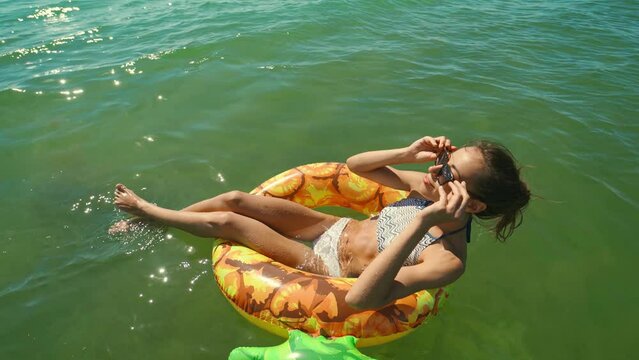 happy smiling young woman in sunglasses swimming on inflatable pineapple floating ring in sea water and laughing. camera zooming out. traveling and summer vacation concept. Ukraine, Odessa region