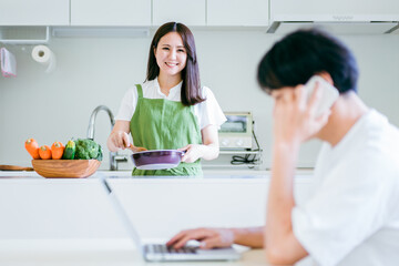 テレワークする男性と料理を作る女性
