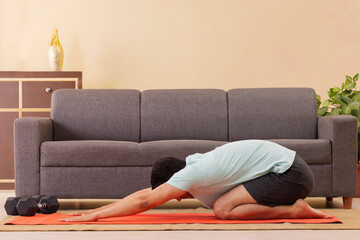Portrait of a young man doing child pose yoga on exercise mat at home