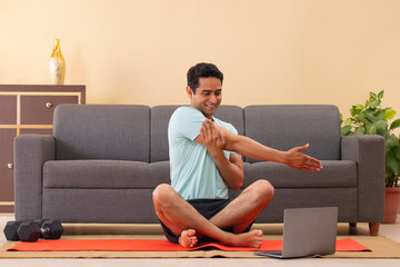 Male Indian Yoga instructor conducting an online class with laptop