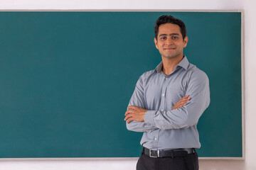 School teacher standing in front of blackboard with arms folded in classroom - obrazy, fototapety, plakaty