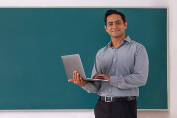 Portrait of a young school teacher using laptop in classroom