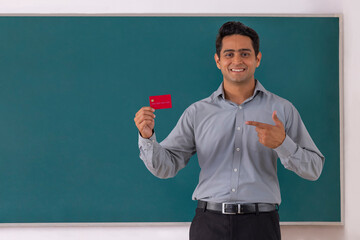 School teacher pointing at credit card while standing in front of blackboard in classroom