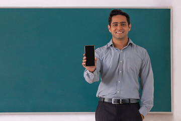 School teacher showing Smartphone while standing in front of blackboard in classroom