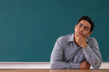 Portrait of a school teacher thinking with hand on chin while sitting classroom