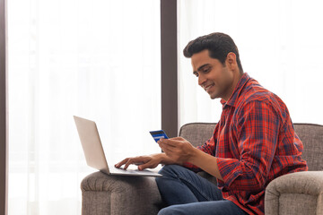 Portrait of a young man shopping online through laptop using credit card