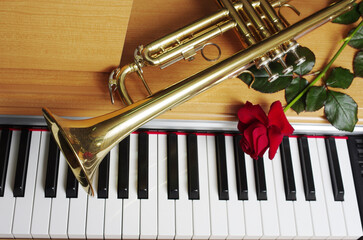 Red rose and trumpet on the piano keyboard.