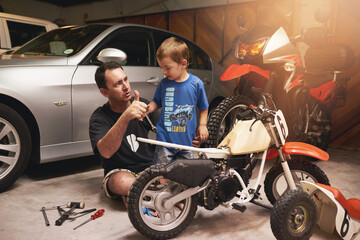 Being a role model to his little boy. Shot of a father and son fixing a bike in a garage.