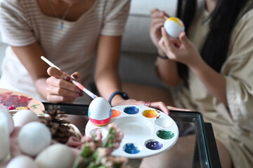 Young woman and her young sister coloring eggs, preparation for the Easter holiday.